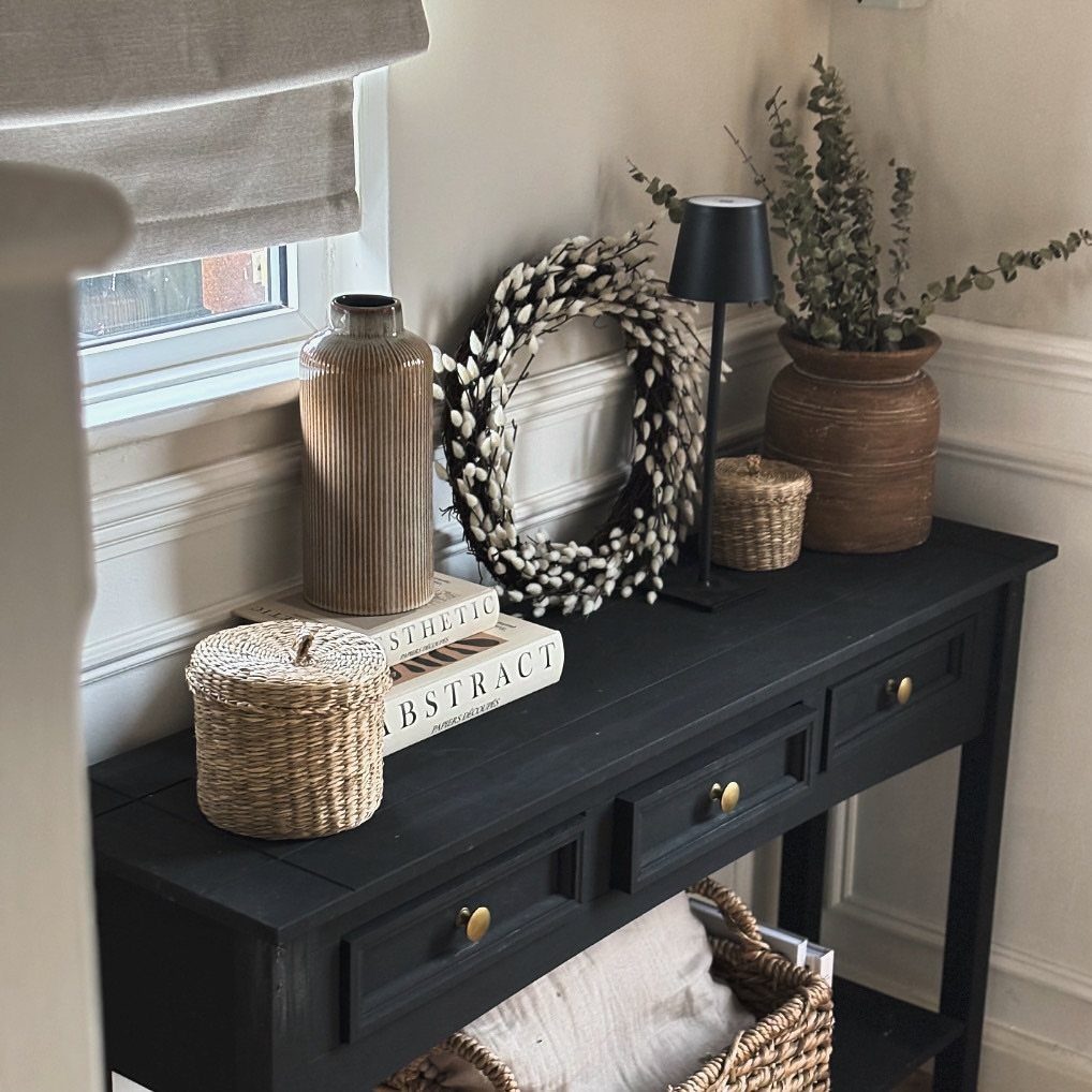 Black console table with drawers styled with a wreath, lamp, and greenery.