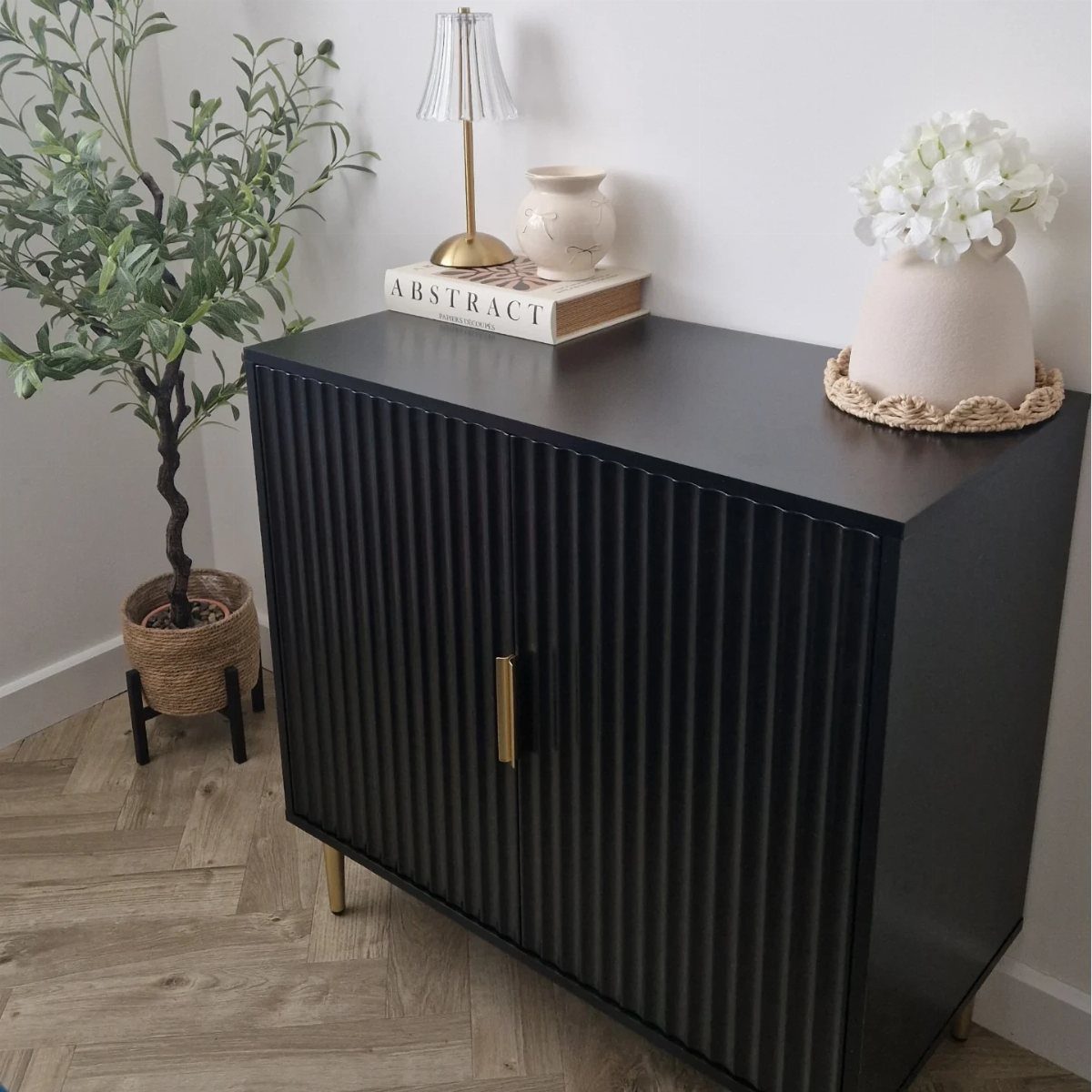 Black fluted console cabinet with gold accents and decorative items on top.