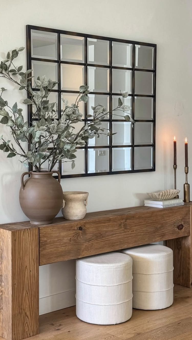 Chunky wood console table with a window-pane mirror and white poufs underneath.