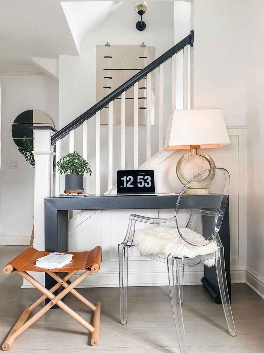Black console table used as a desk with a clear acrylic chair and lamp.