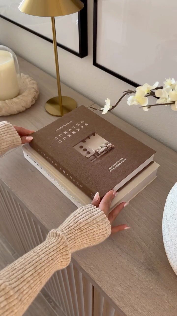 Hands placing a stack of books on a light wood fluted console table.