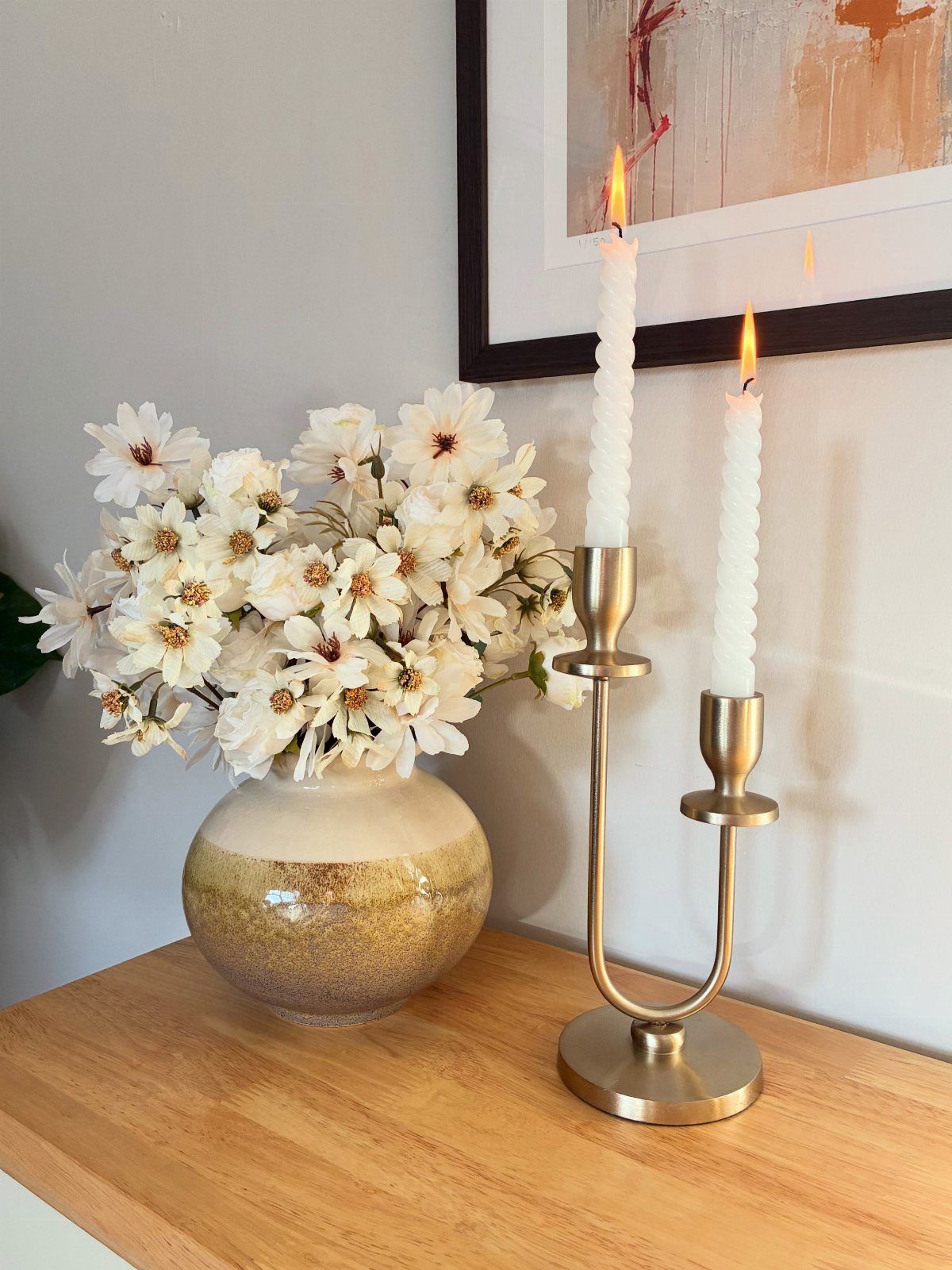Wooden console table with white flowers in a gold vase and lit taper candles.