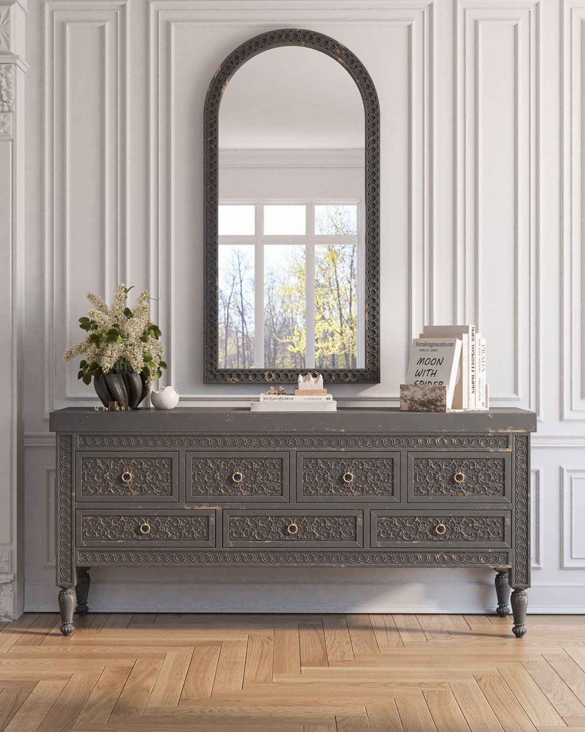 Grey ornate console table with drawers and an arched mirror on a white wall.