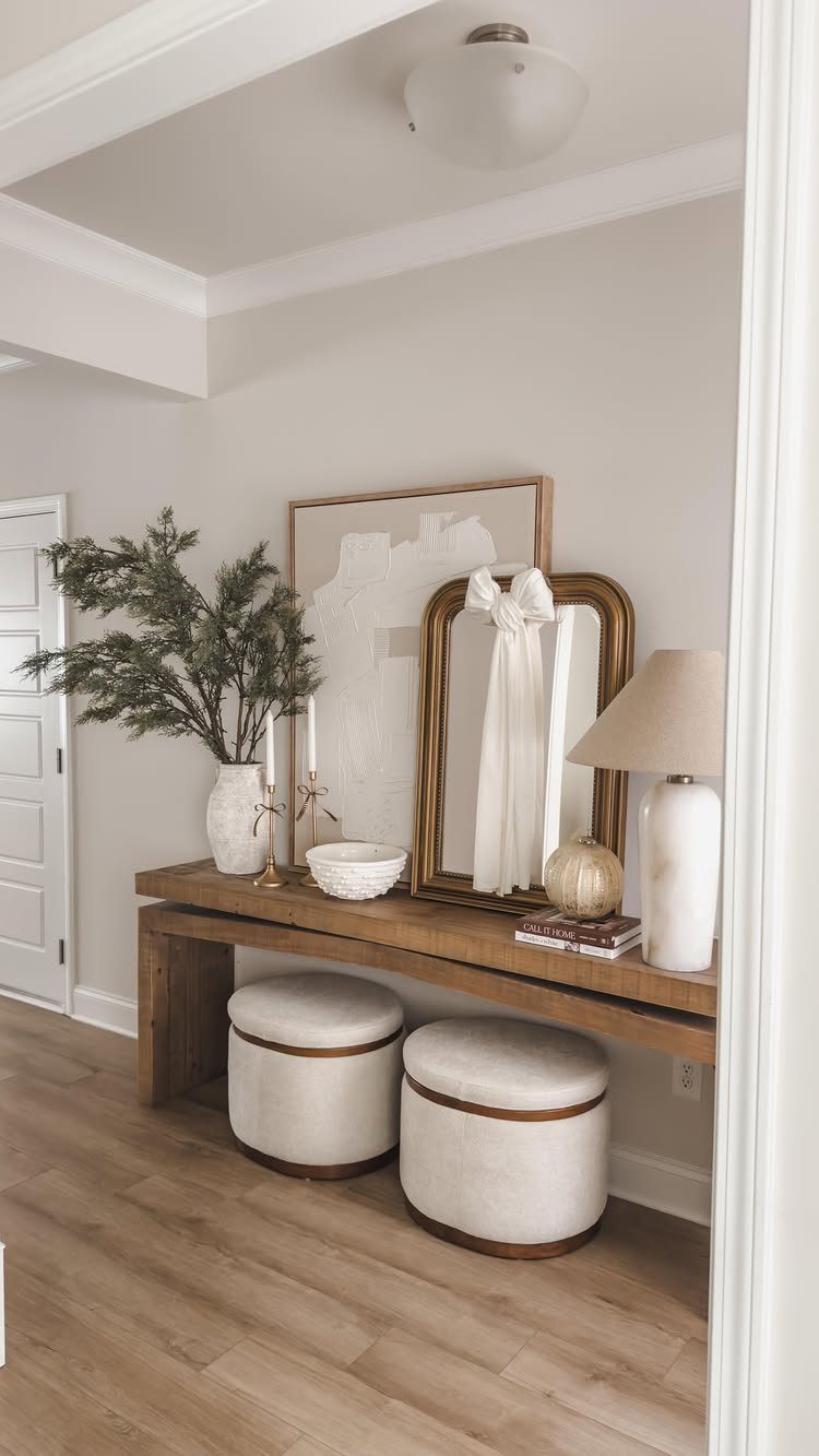 Wood console table with two white cylindrical ottomans tucked underneath in a bright room.