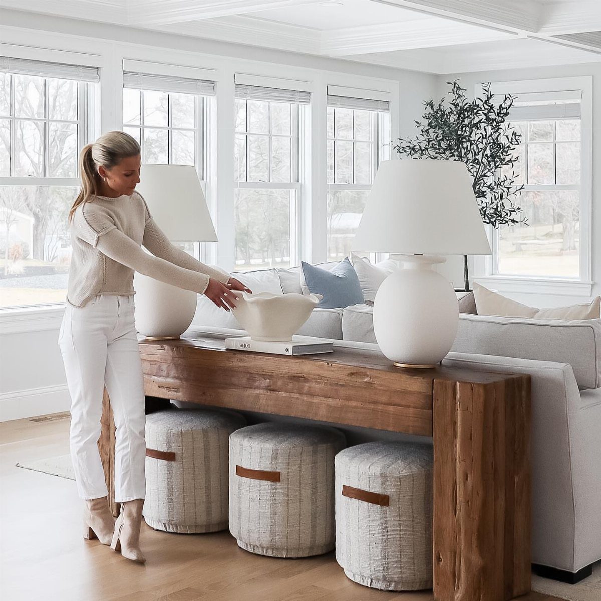 Chunky wood console table with three grey poufs tucked underneath behind a sofa.