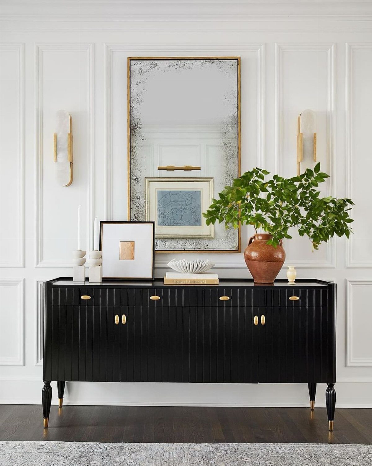 Black fluted console table with gold accents and wall sconces against white paneling.