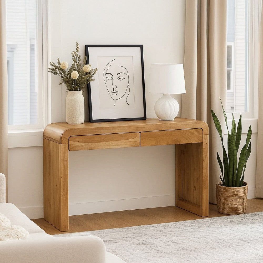 Light wood console table with drawers featuring a lamp, framed art, and a plant.