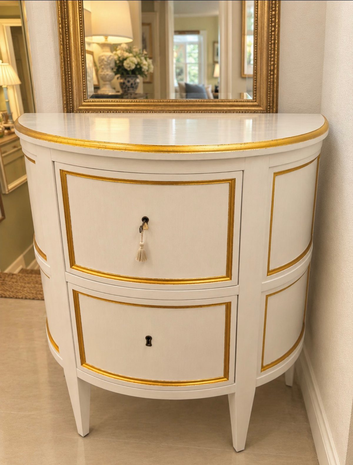 White demilune console table with gold trim and a gold-framed mirror above.