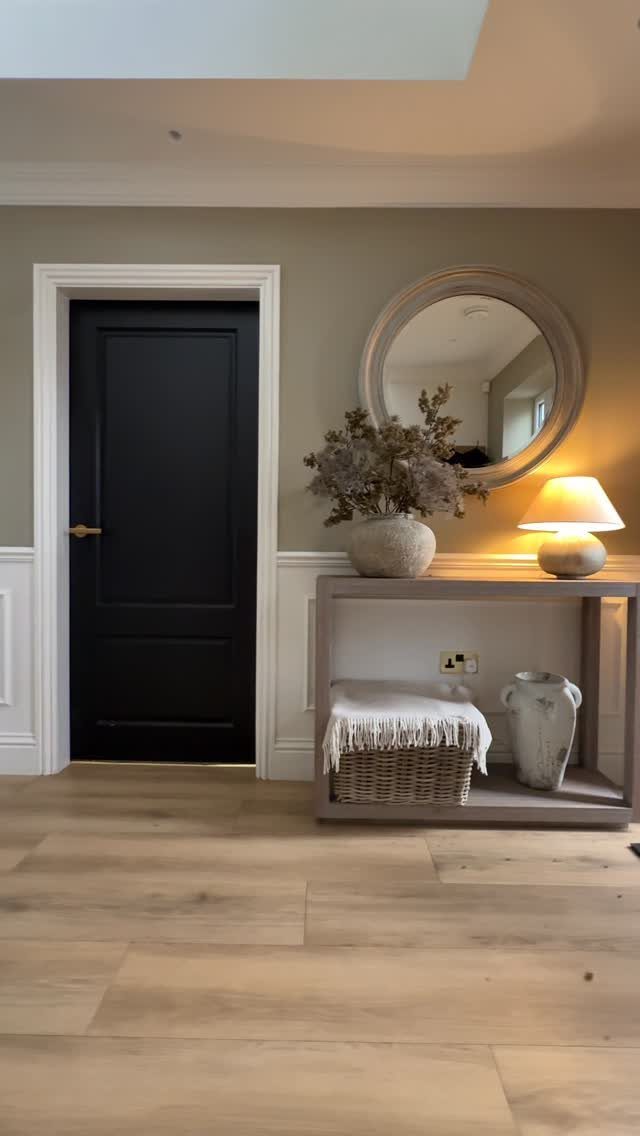 Grey console table with a round mirror and lamp in a hallway setting.