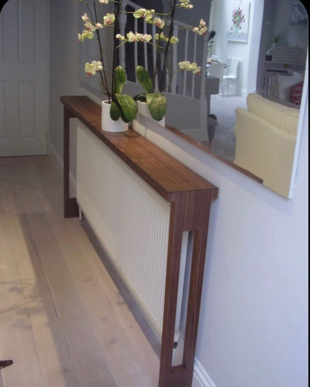 Narrow wood console table over a white radiator with yellow orchids and mirror.