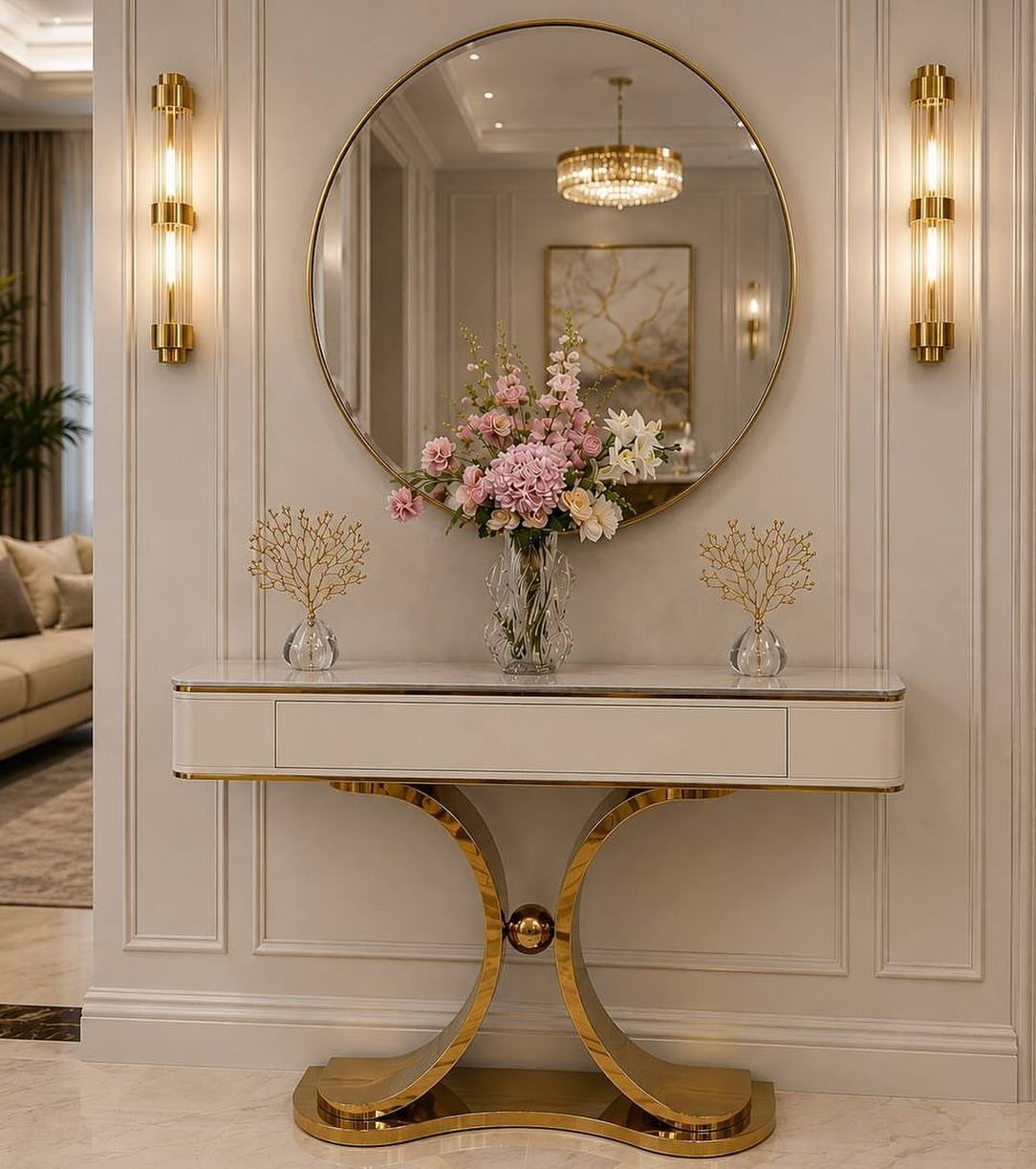Round gold mirror hanging above a white and gold console table with flowers.