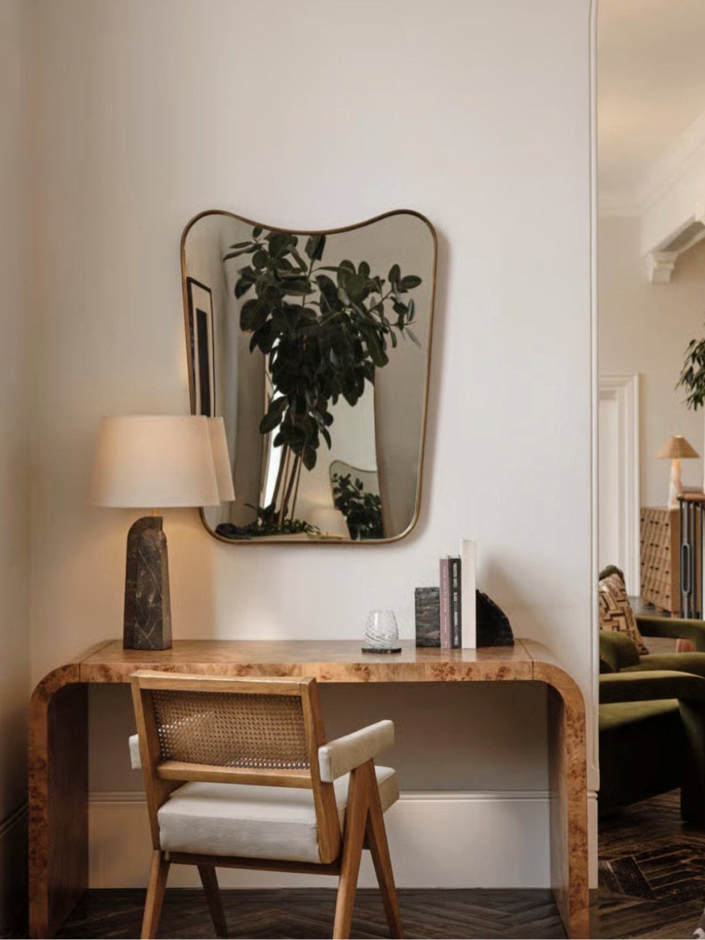 Waterfall wood console table used as a desk with a cane-back chair and mirror.