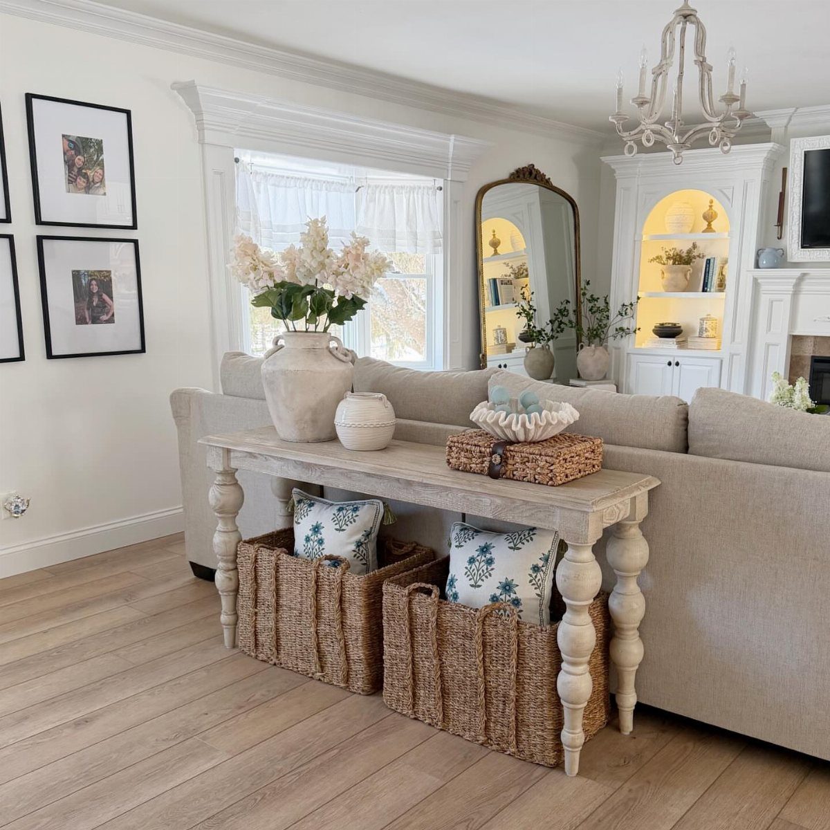 Light wood console table behind a sofa with two woven baskets underneath.