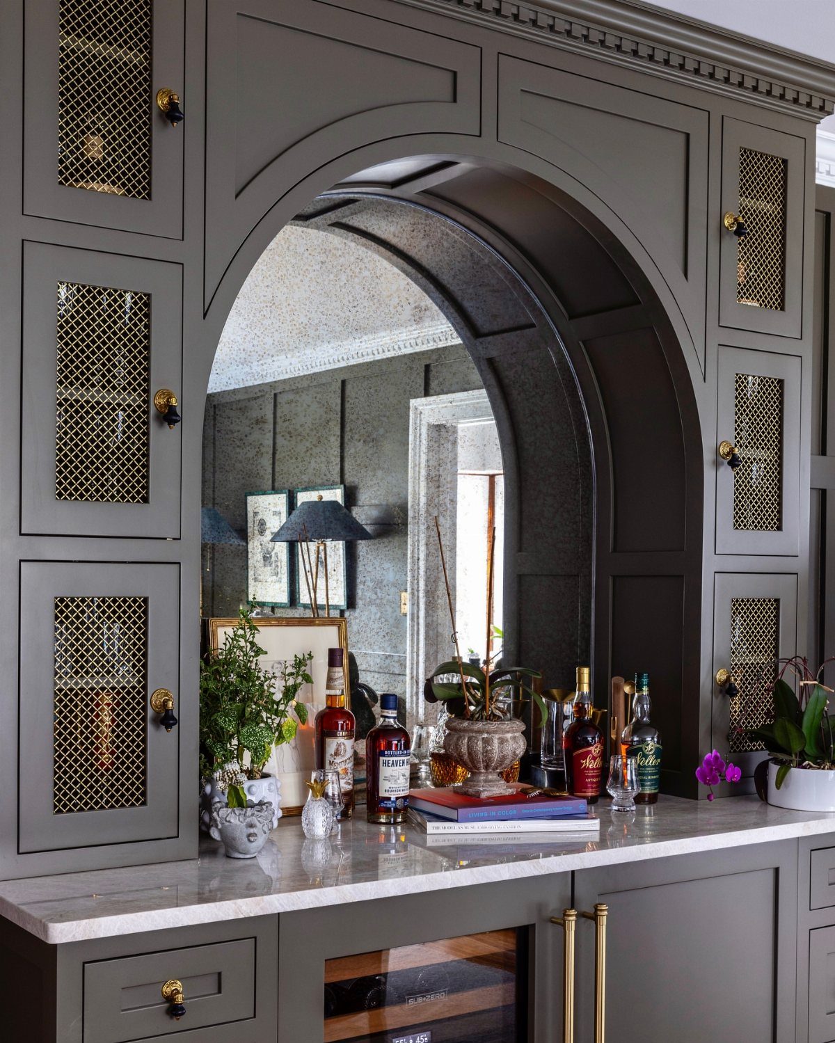 Gray built-in corner bar cabinet with an arched mirror and integrated wine cooler.