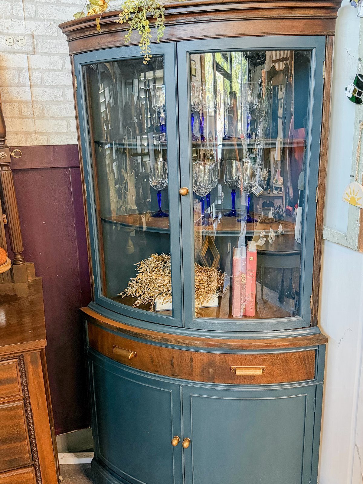 Curved blue-green corner cabinet with glass doors and natural wood trim accents.