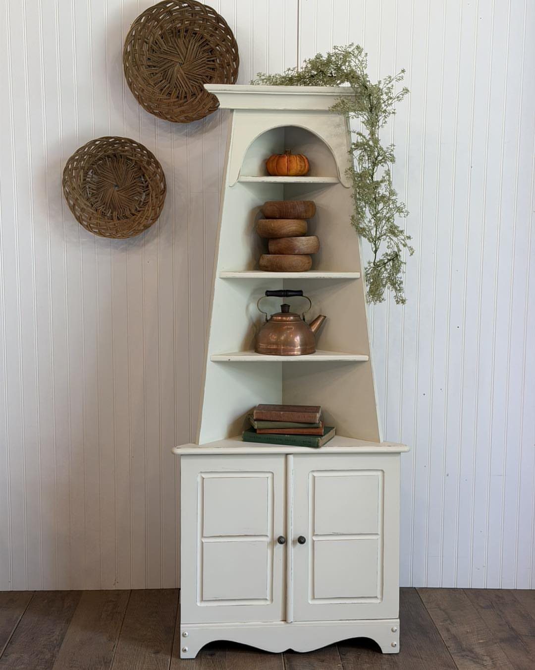 White farmhouse corner cabinet with open shelving and a bottom cupboard against a wall