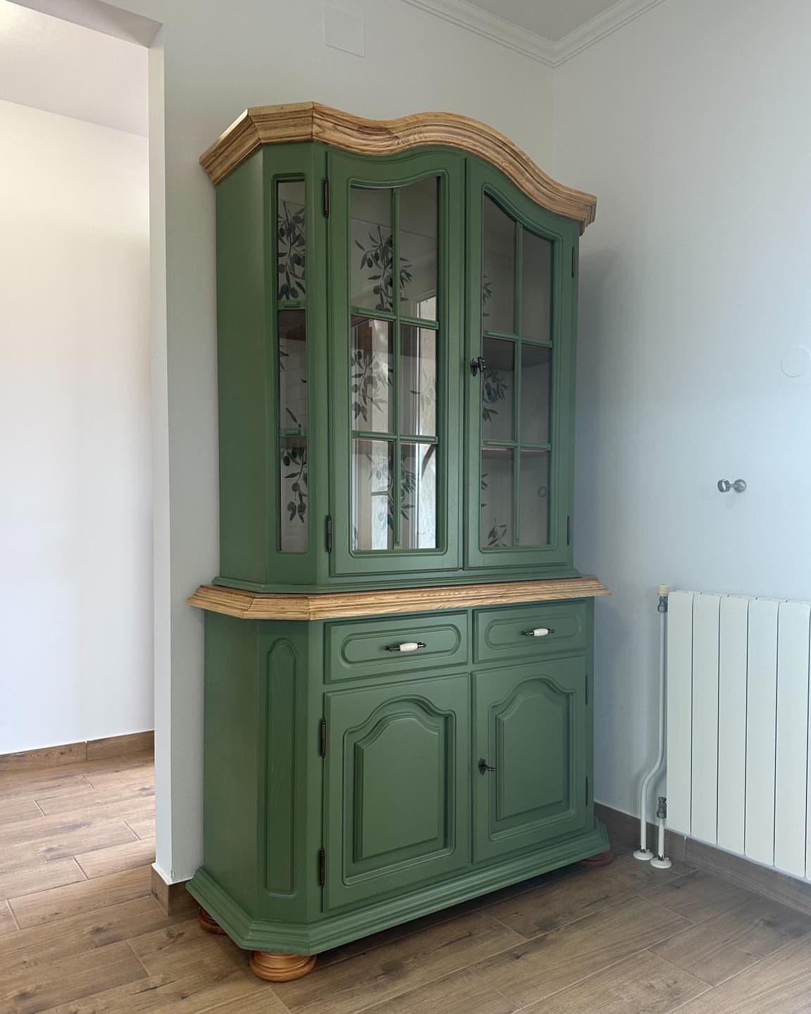 Green corner cabinet with glass doors and light wood trim in a dining room.