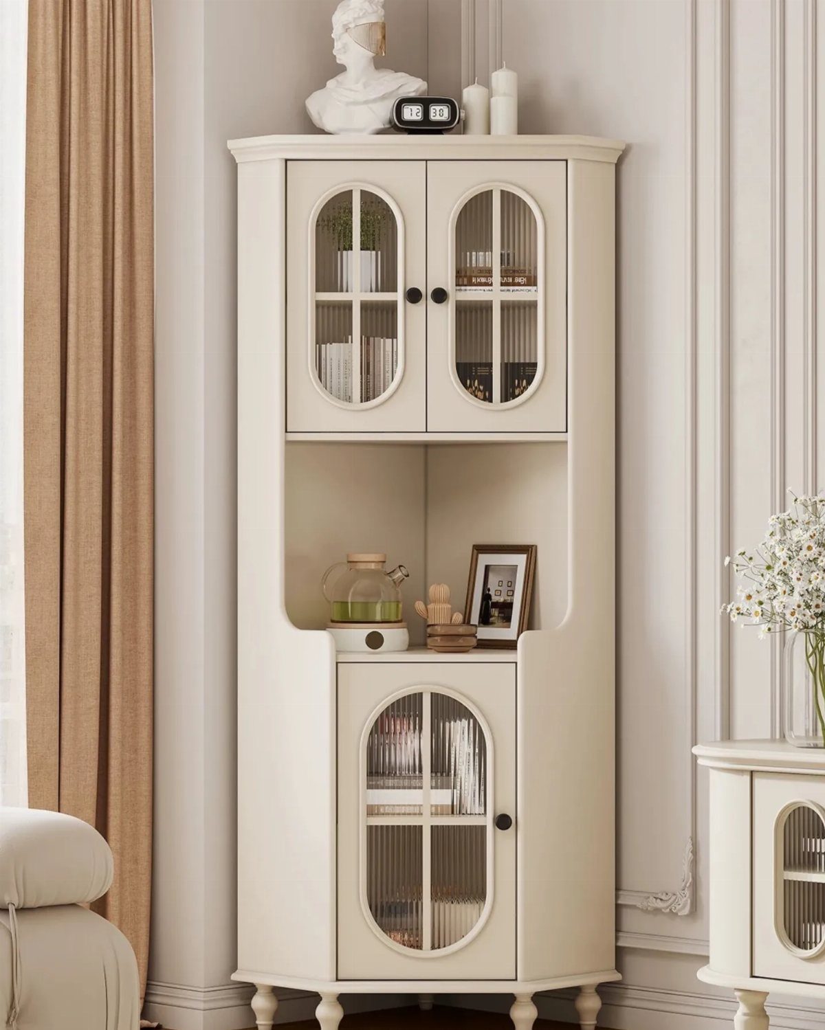 Tall cream corner cabinet with glass doors and open shelving in a bright room.