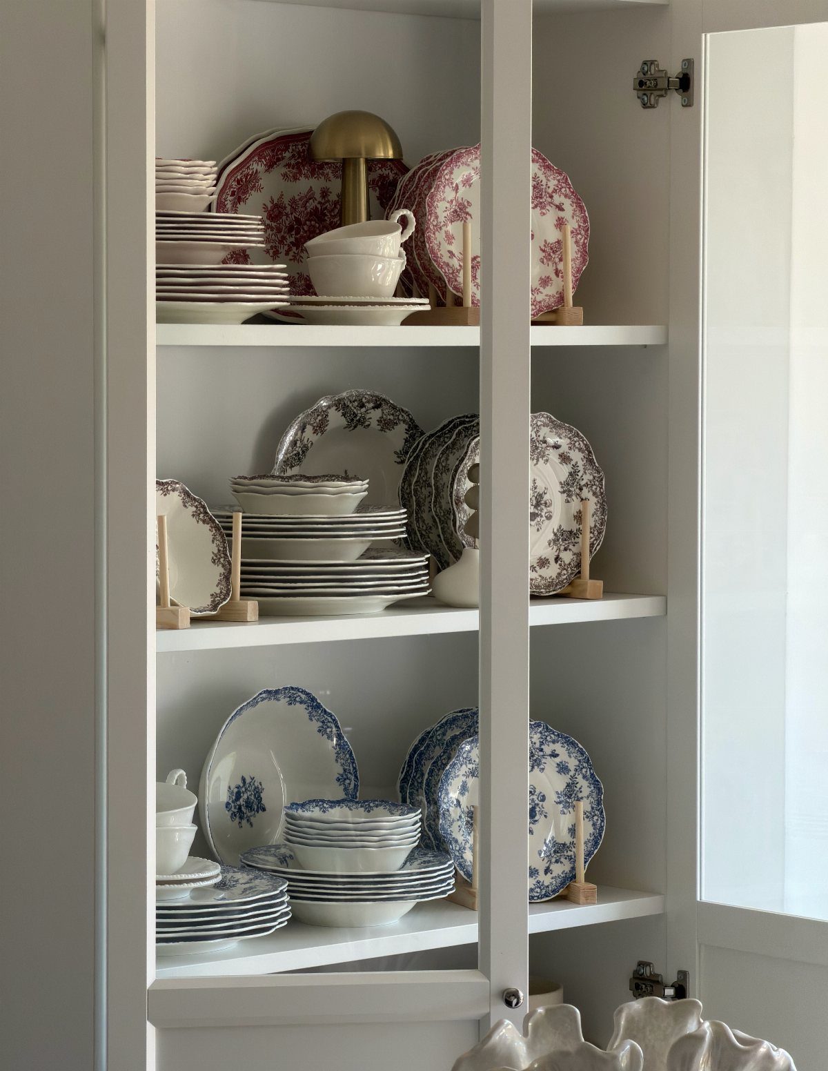 White corner cabinet shelves displaying vintage patterned plates and bowls in various colors.