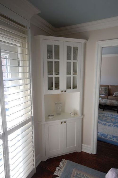 White built-in corner cabinet with glass doors and lower storage in a dining area.