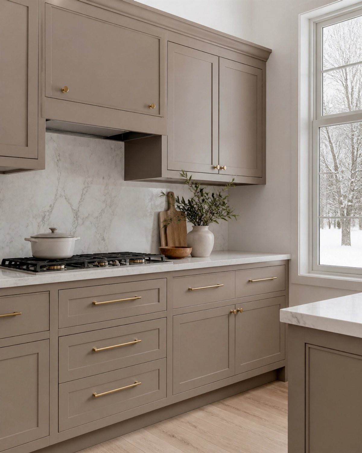 Taupe shaker kitchen cabinets with gold hardware and white marble countertops.