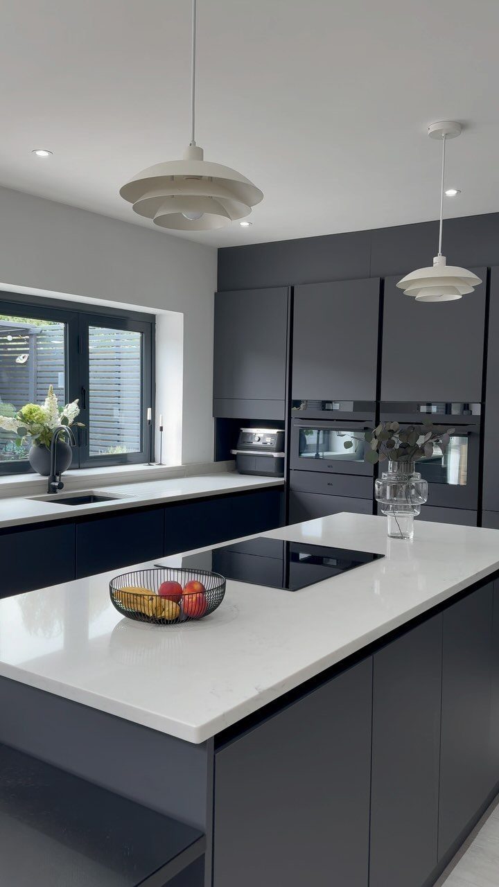 Modern kitchen with dark charcoal grey cabinets and white quartz countertops and island.