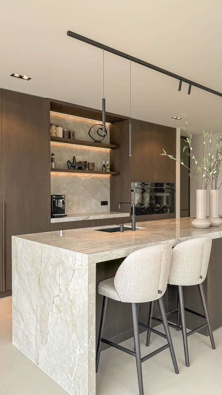 Thick marble waterfall island with dark wood cabinets and grey bar stools.
