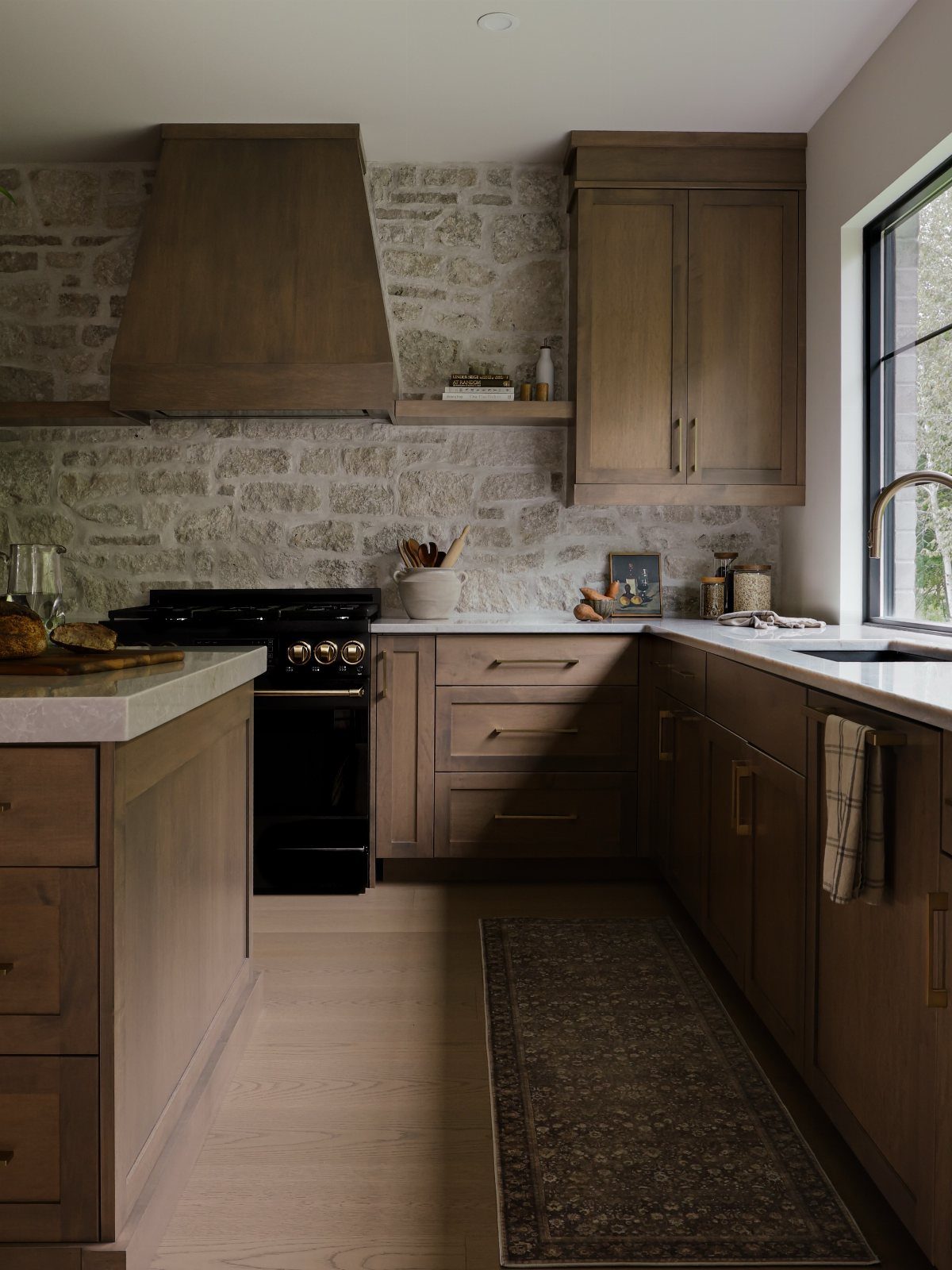 Dark wood kitchen cabinets and range hood against a light stone brick wall.