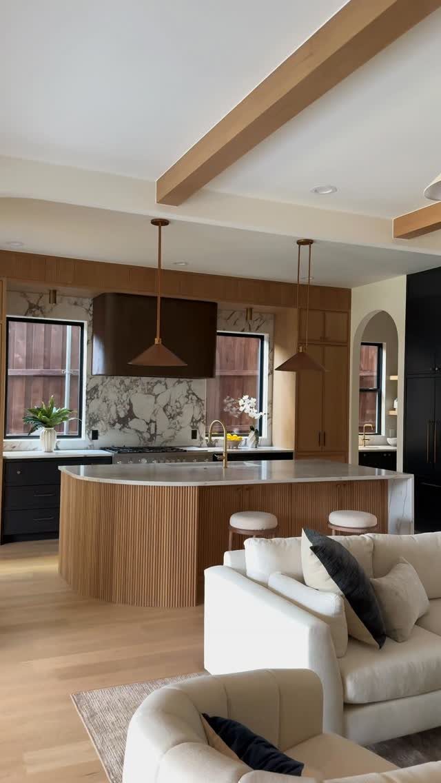 Modern kitchen with curved wood island, dark cabinets, and white neutral living area.