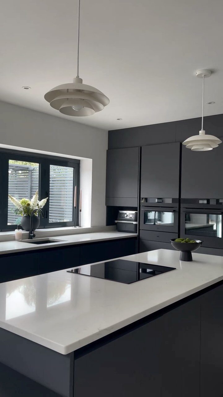 Modern kitchen with dark gray cabinets, white countertops, and white pendant lighting.