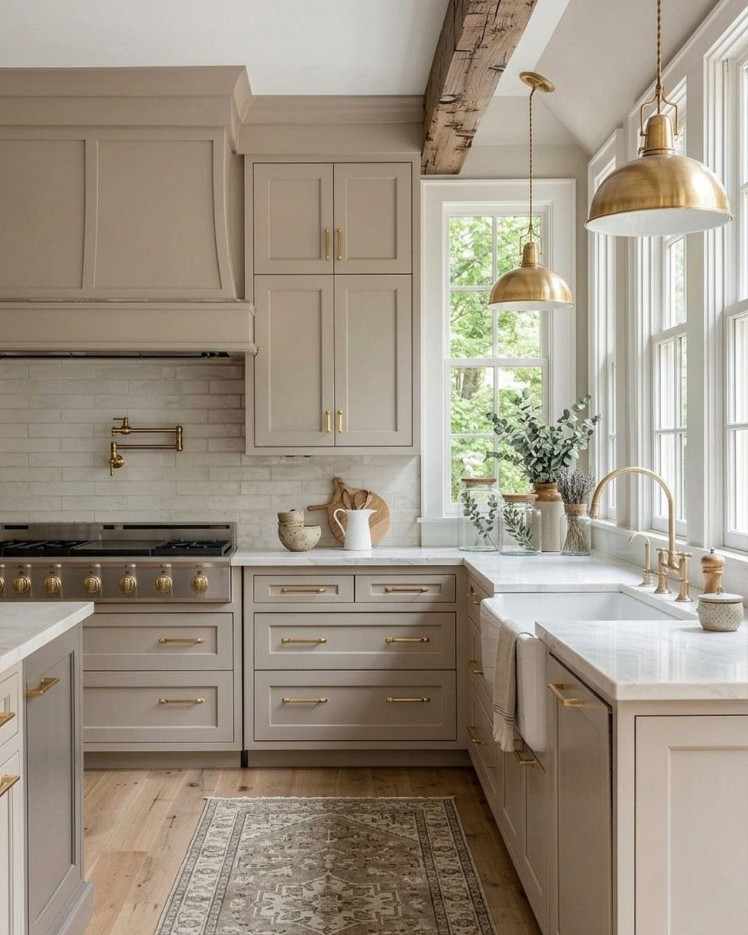 Taupe kitchen cabinets with gold hardware, white countertops, and gold pendant lighting.