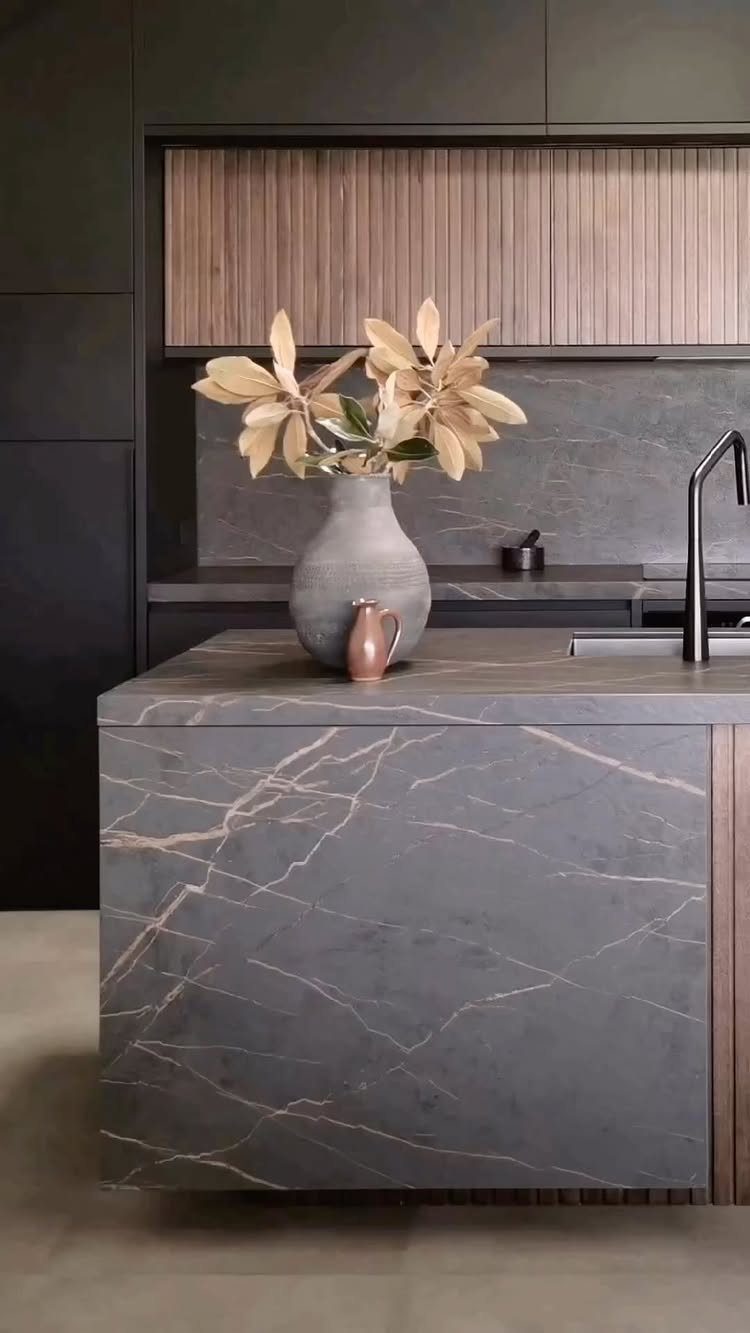 Dark gray matte kitchen island with marble veining and wood slat cabinetry.
