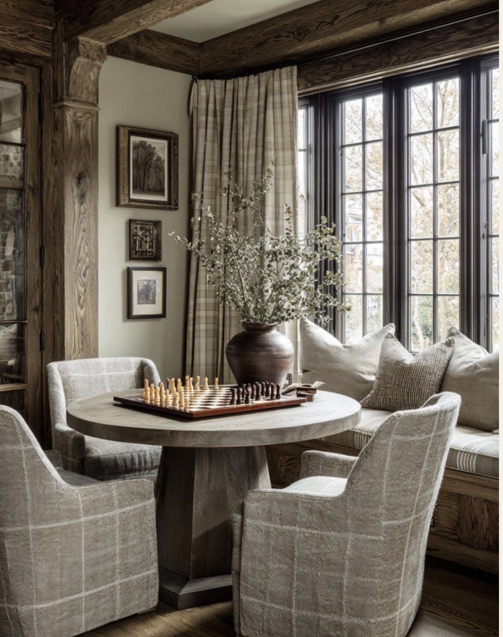 Plush grey plaid armchairs and a cushioned bench around a round wooden dining table.