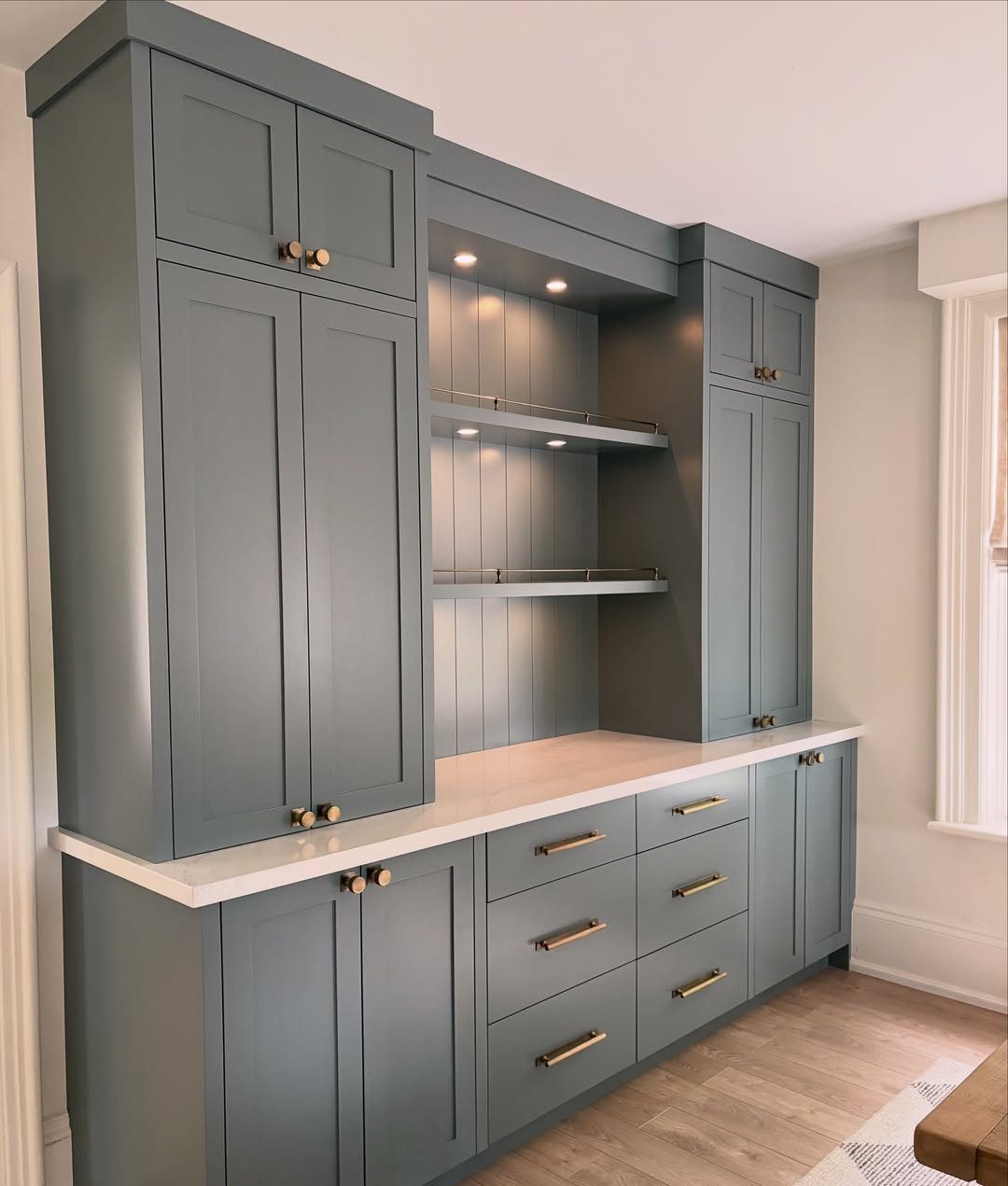 Blue-grey built-in dining room storage unit with white countertop and gold hardware.