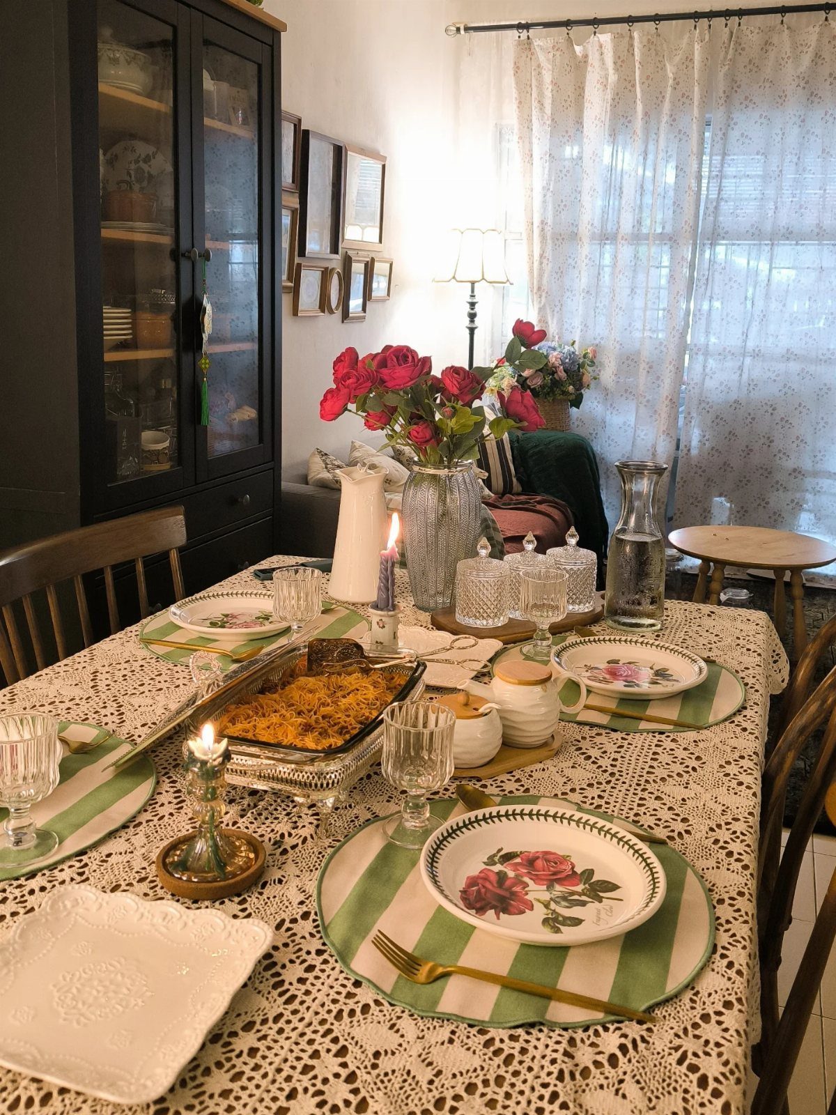 Dining table with red roses in a vase and floral plate settings.