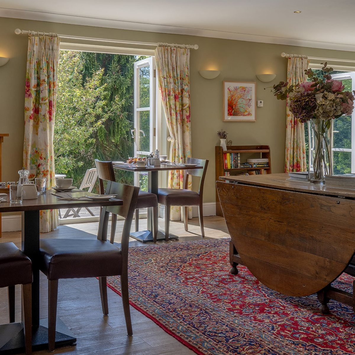 Bright dining room with open French doors leading to a green garden and red rug.