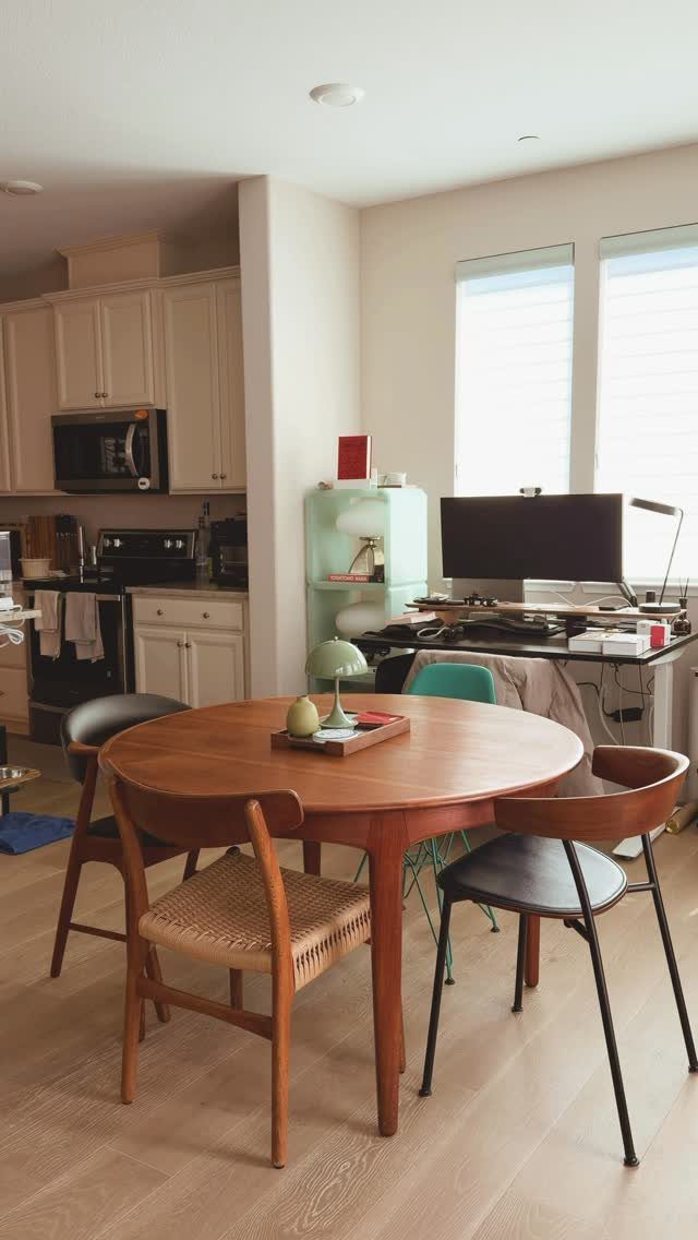 Round wooden dining table with a variety of mismatched chairs in a bright room.
