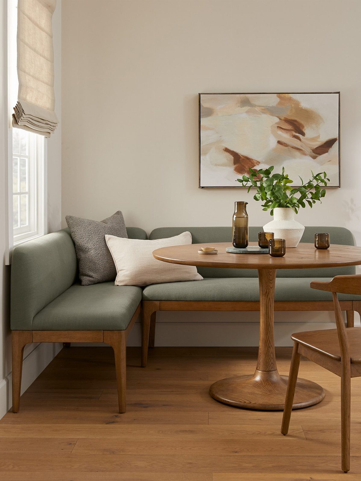 Green upholstered corner dining bench with pillows and a round wooden table.