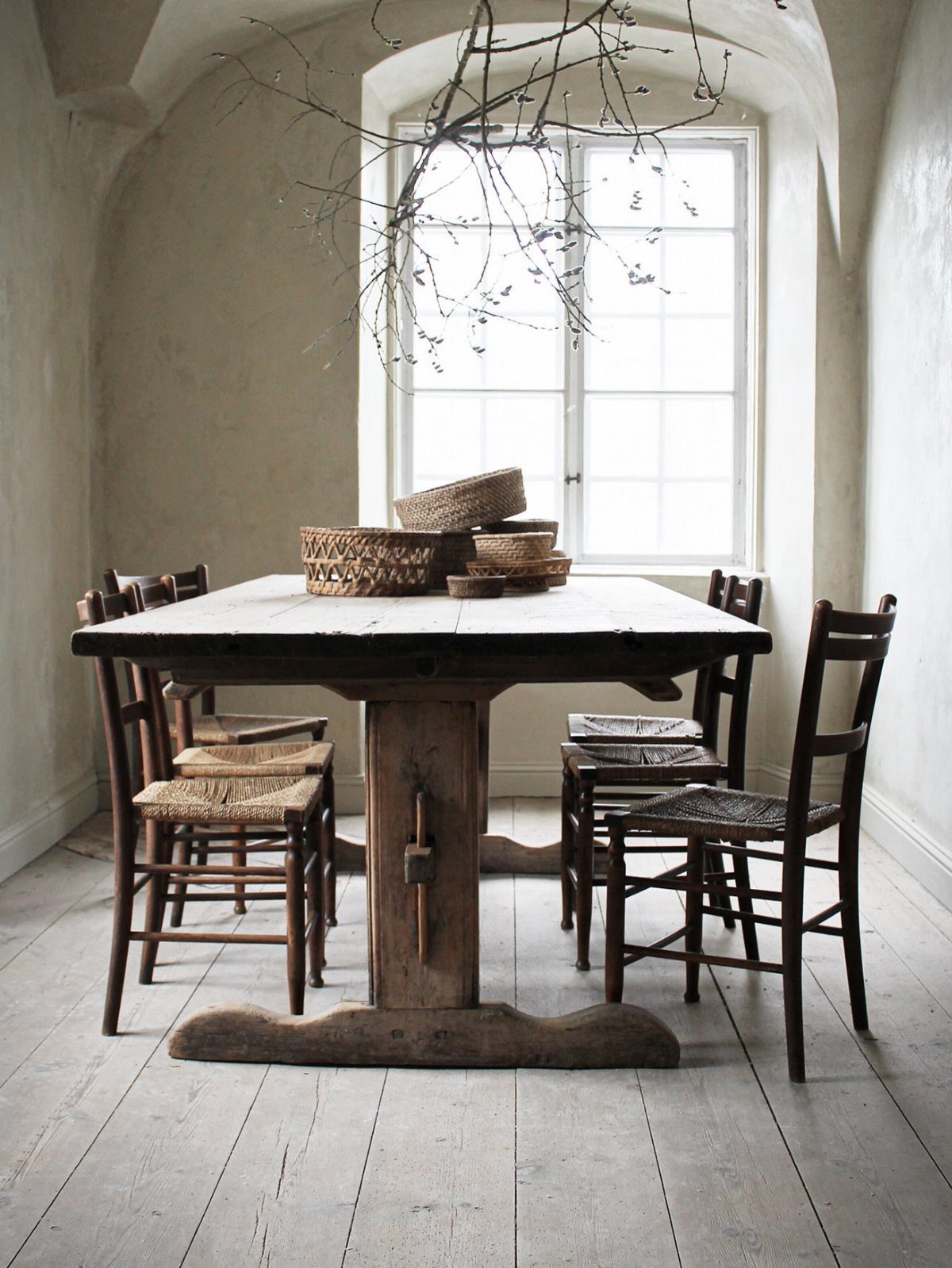 Rustic wooden dining table and chairs in a bright, white-walled cottage room.