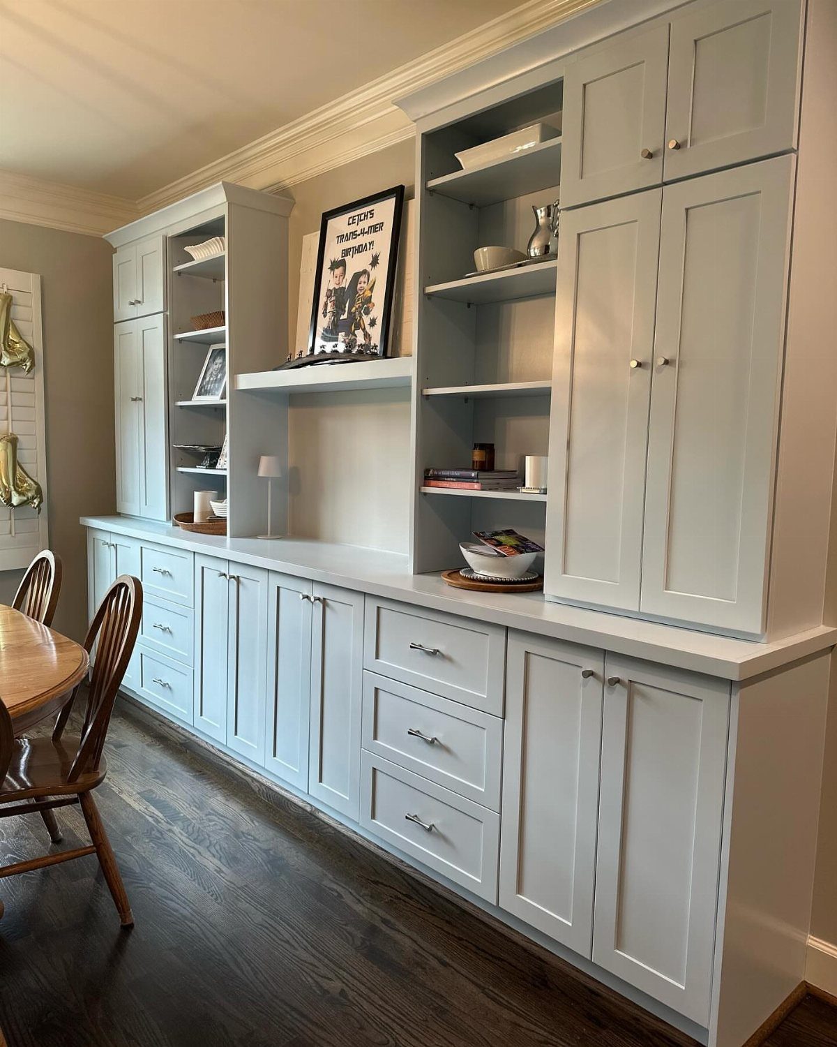 Light grey built-in shelving and cabinetry unit against a wall with dark hardwood floors.