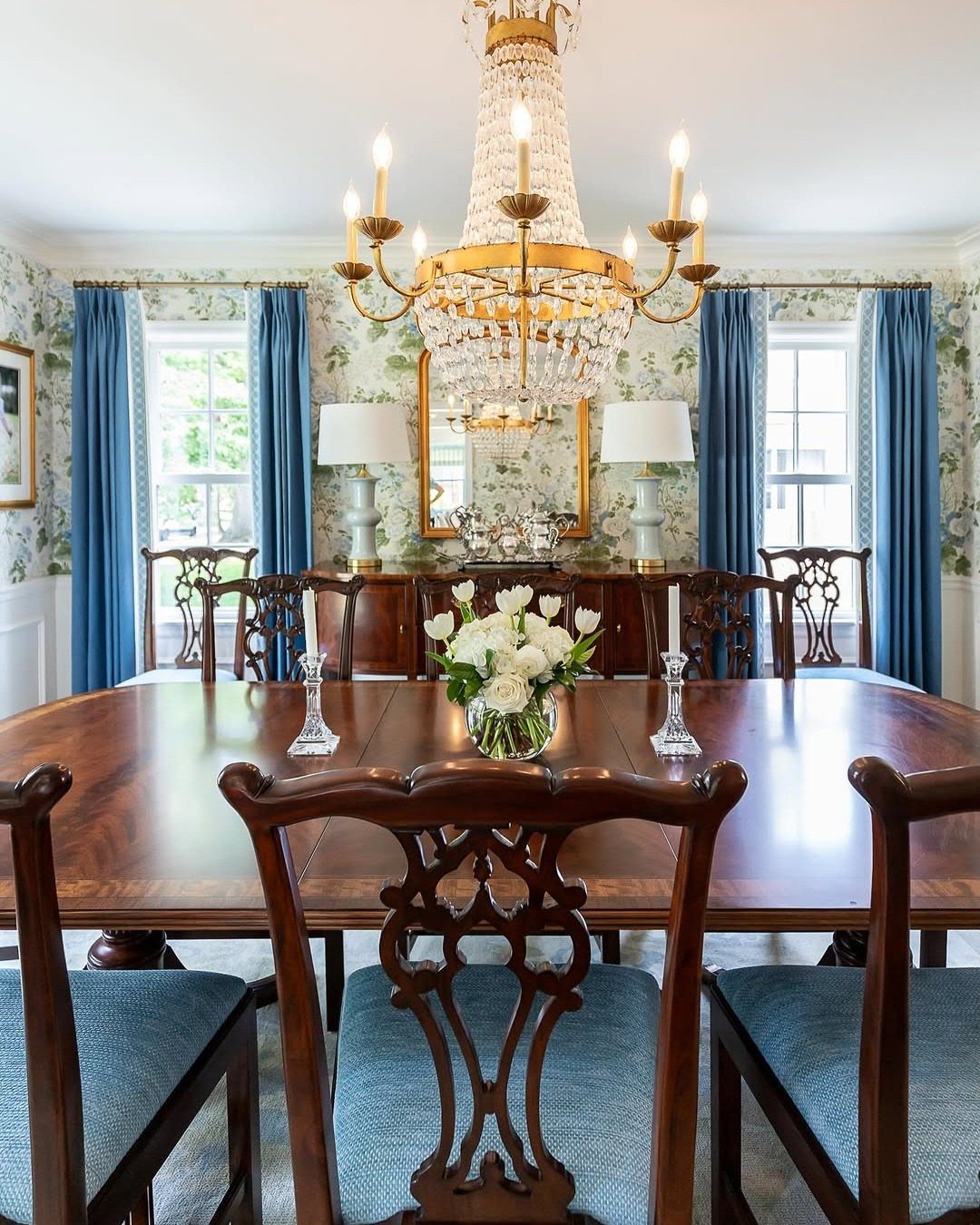 Dining room with floral wallpaper, a crystal chandelier, and a wooden dining table.