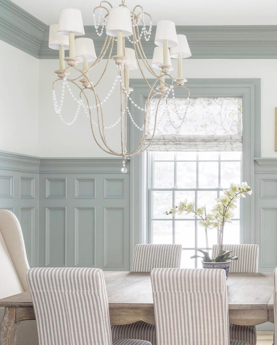 Dining room with light blue wainscoting, striped chairs, and a crystal chandelier.