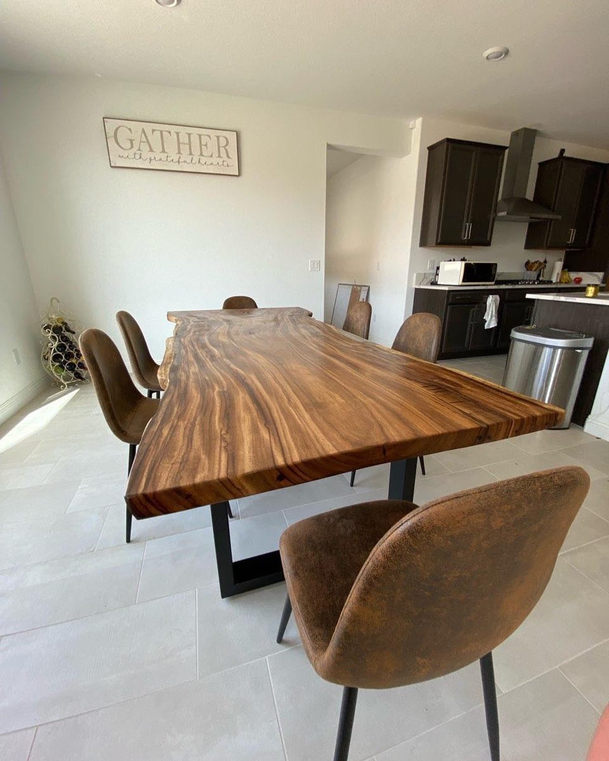 Live-edge wooden dining table with brown upholstered chairs in a bright modern room.