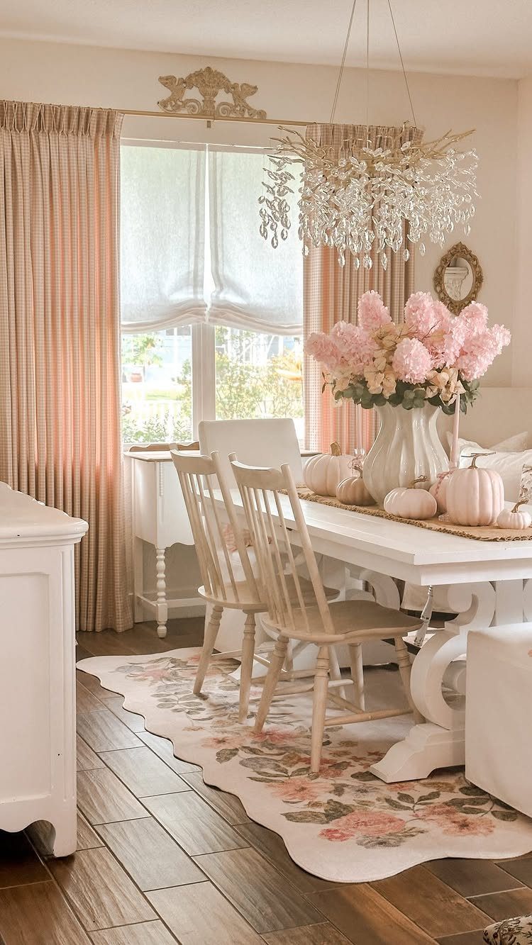 White dining table and chairs with a floral rug and crystal chandelier.