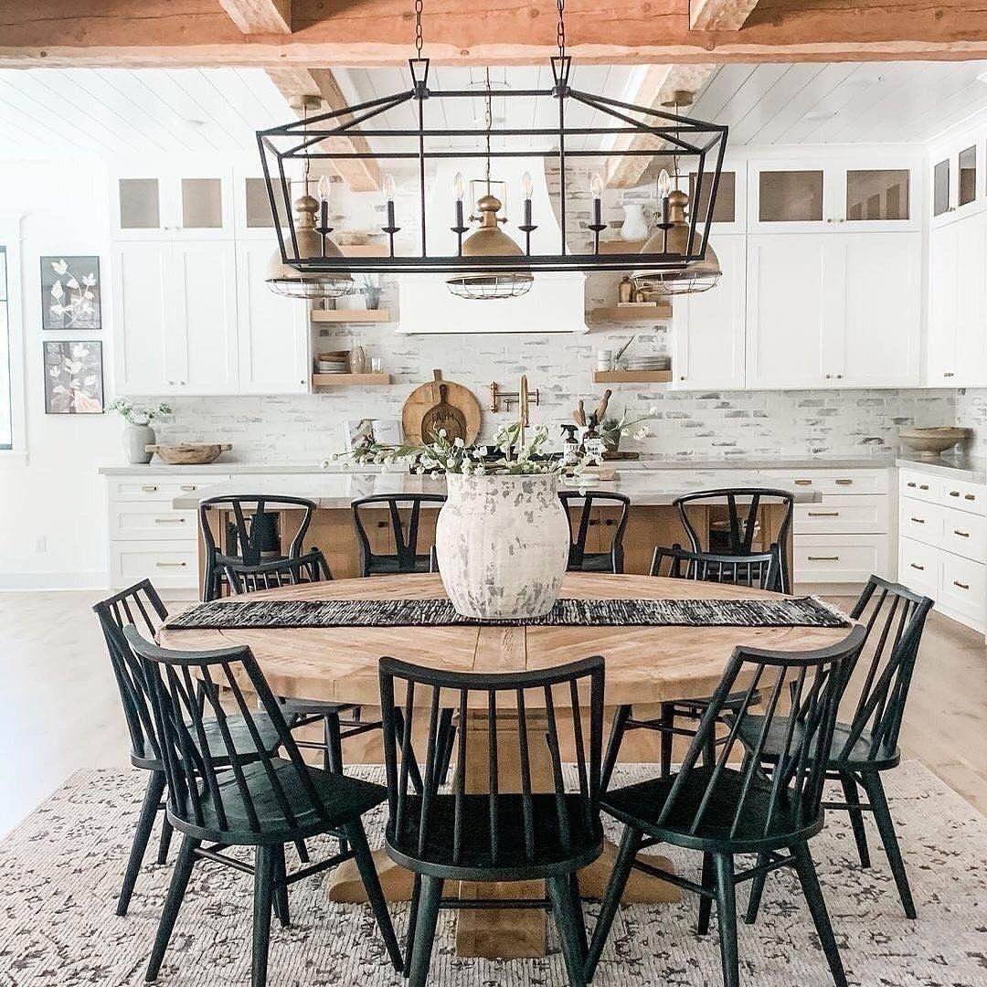 Round light-wood dining table with black chairs under a large black metal chandelier.