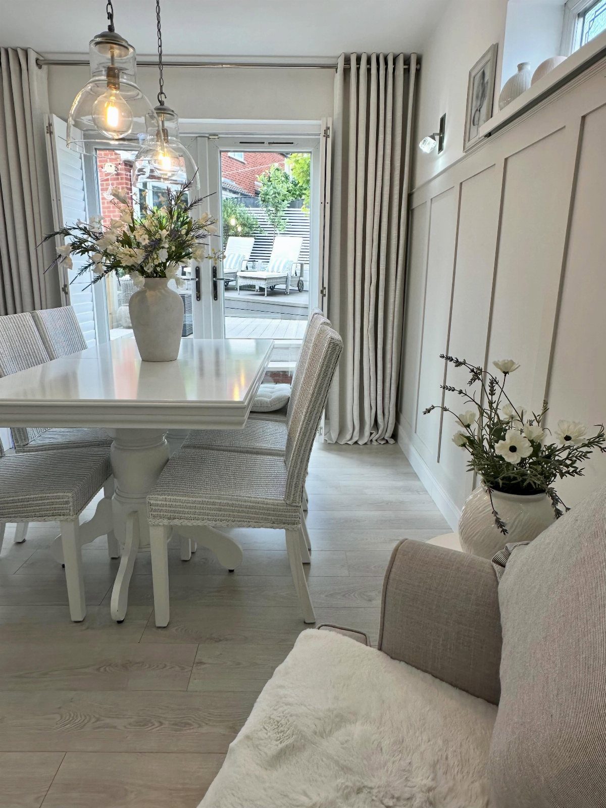 White dining room with paneled walls, light wood floors, and patterned chairs.