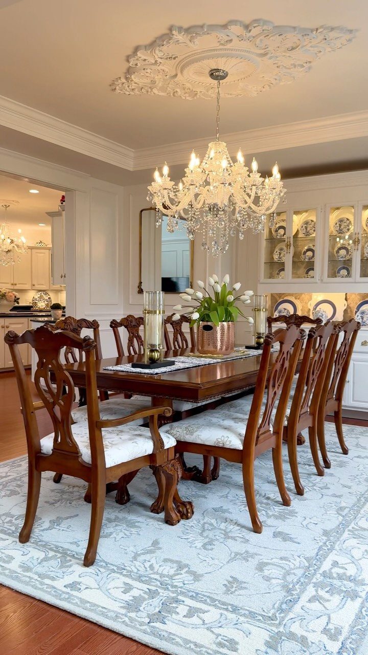 Light blue patterned area rug under a wooden dining table and crystal chandelier.