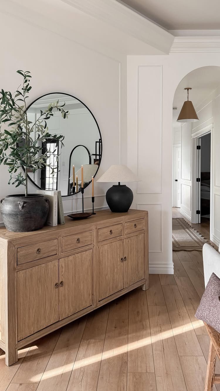 Wooden sideboard with a round mirror, black lamp, and plant in a bowl.