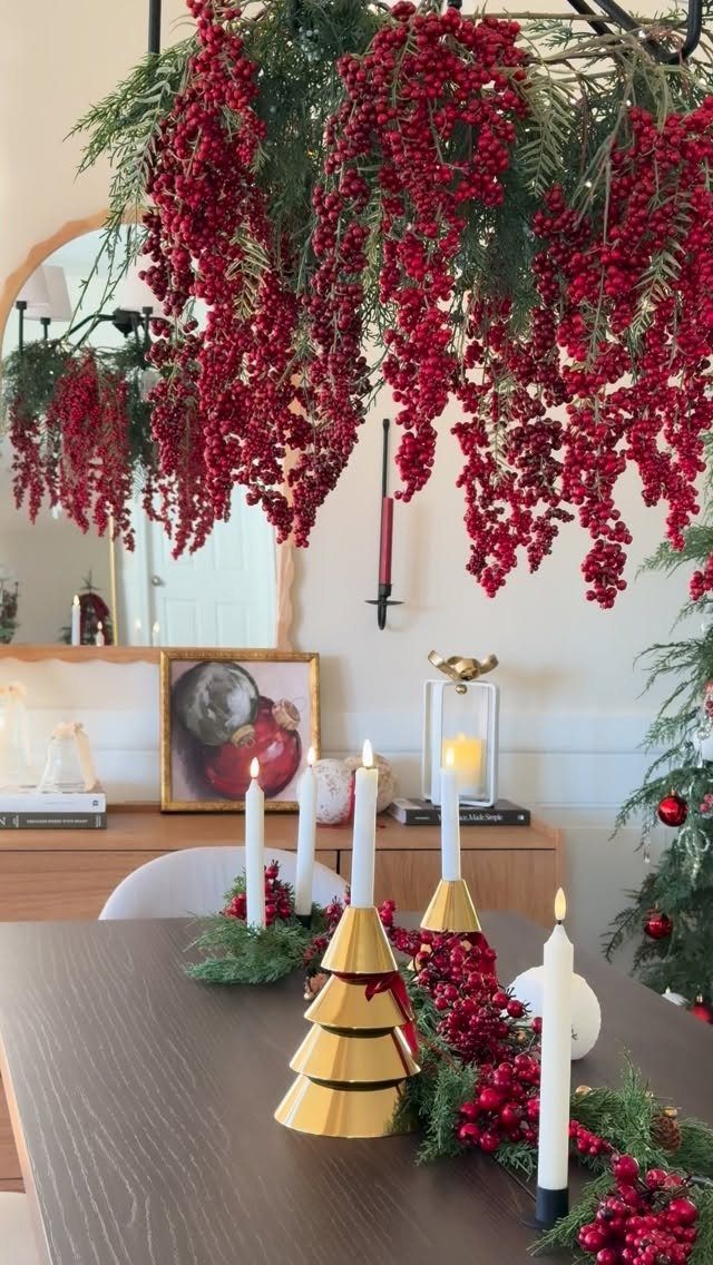 White taper candles in gold holders on a dining table with red berries.