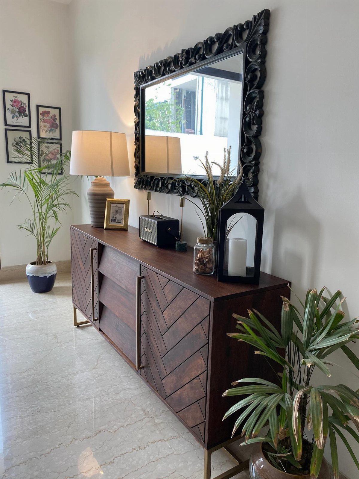 Dark wood chevron sideboard with a large ornate black mirror and decorative lamp.